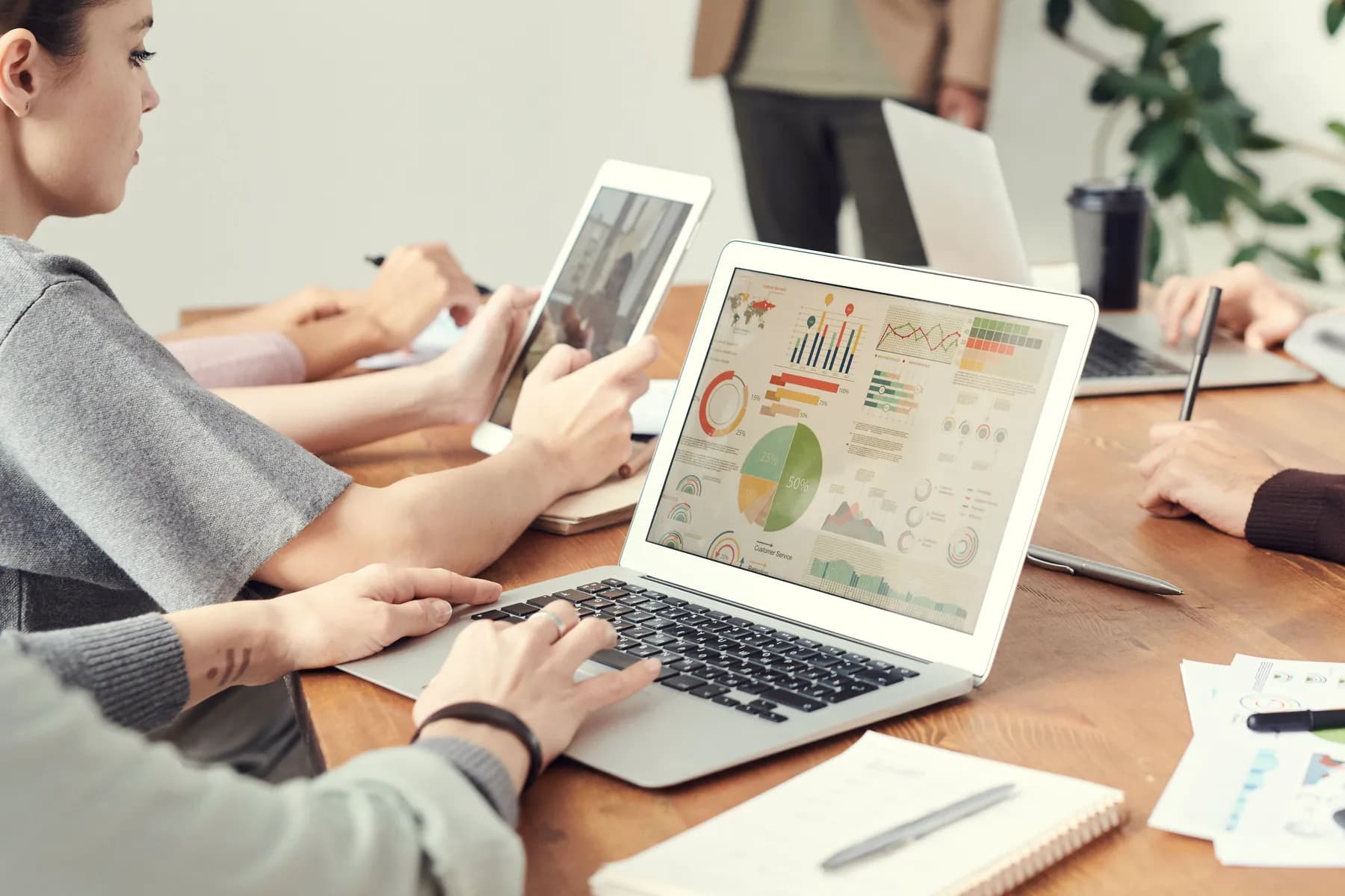 Colleagues at a wooden table work through charts on a laptop and a tablet.