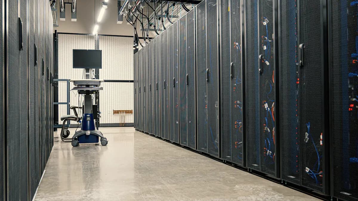 An aisle between two rows of server racks, with a monitor on a wheeled cart at the far end.